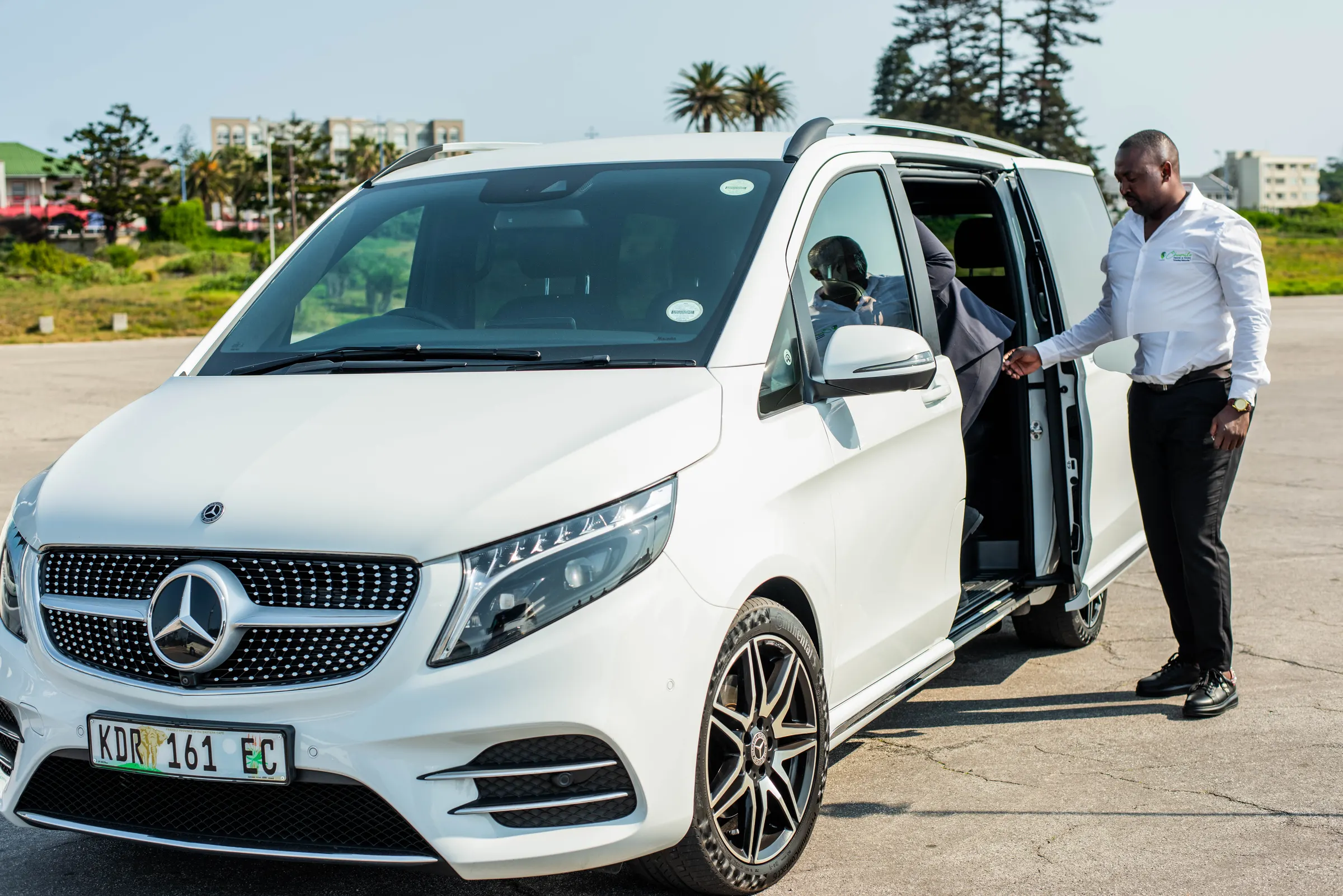 A Chumile chauffeur opening the door of a white Mercedes-Benz V-Class